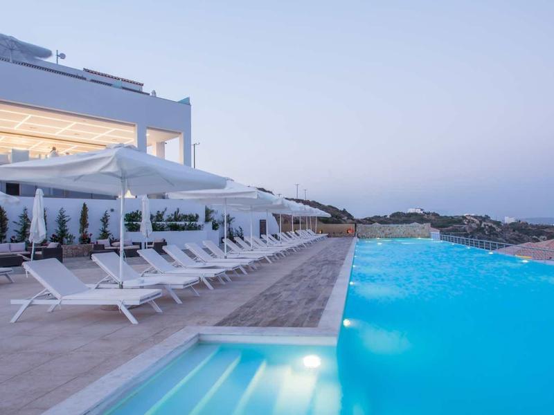 Luksusowy basen typu infinity z leżakami przed nowoczesnym budynkiem o zachodzie słońca.