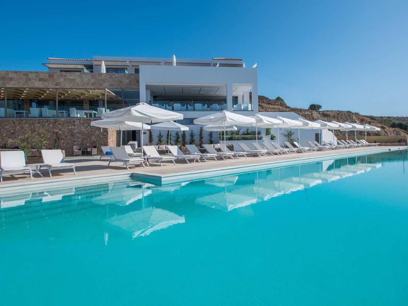 Nowoczesny basen hotelowy z licznymi leżakami i parasolami pod czystym niebem.