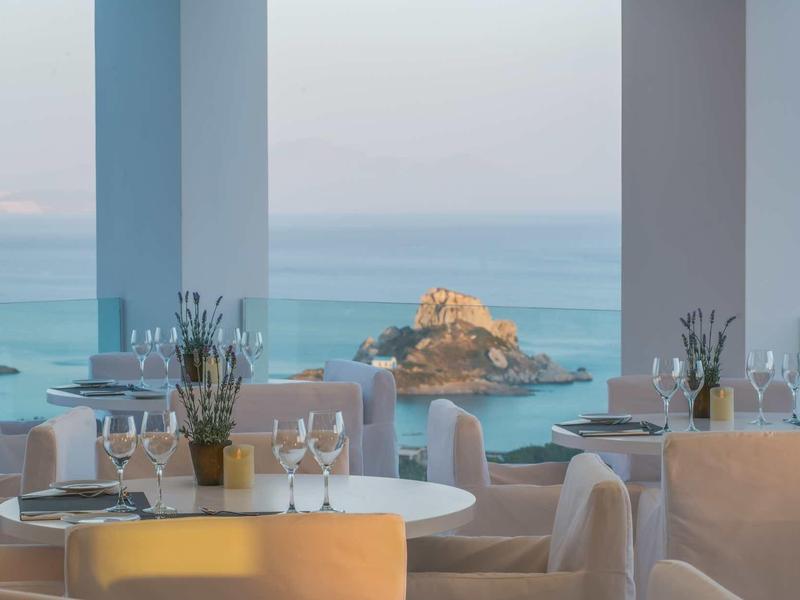 Jasno urządzo­na restauracja z widokiem na morze i skały w oddali.