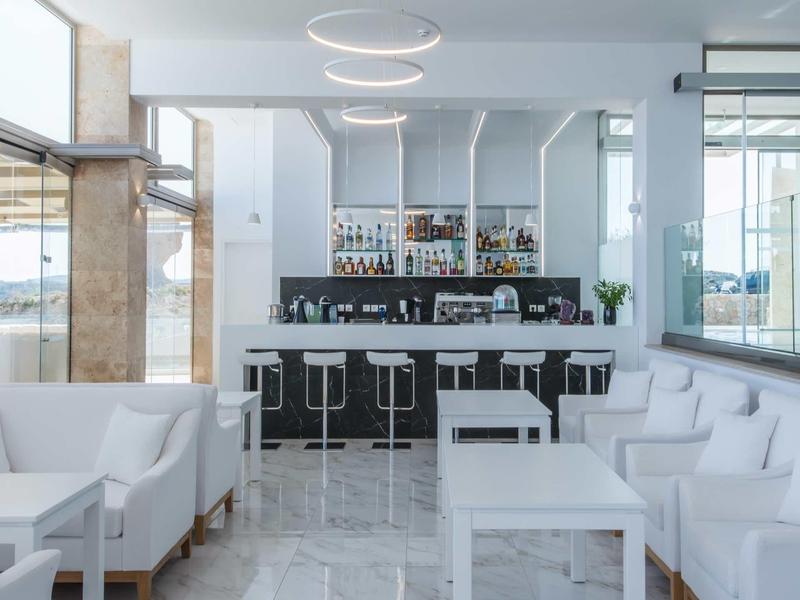 Nowoczesny bar hotelowy z białymi meblami i stylowymi okrągłymi lampami sufitowymi.