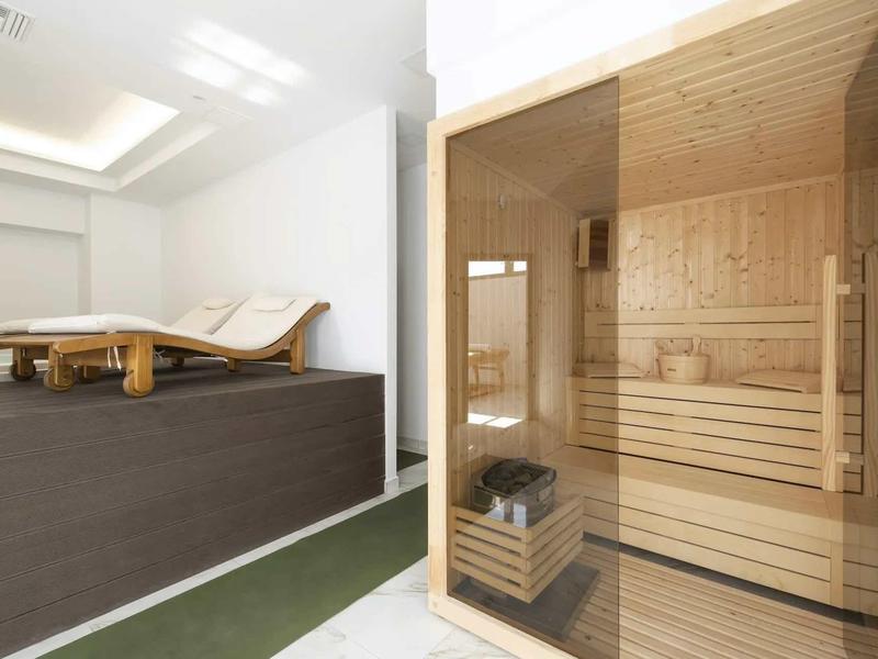 Jasna strefa wellness z drewnianą sauną i dwoma leżakami w spokojnym pomieszczeniu.