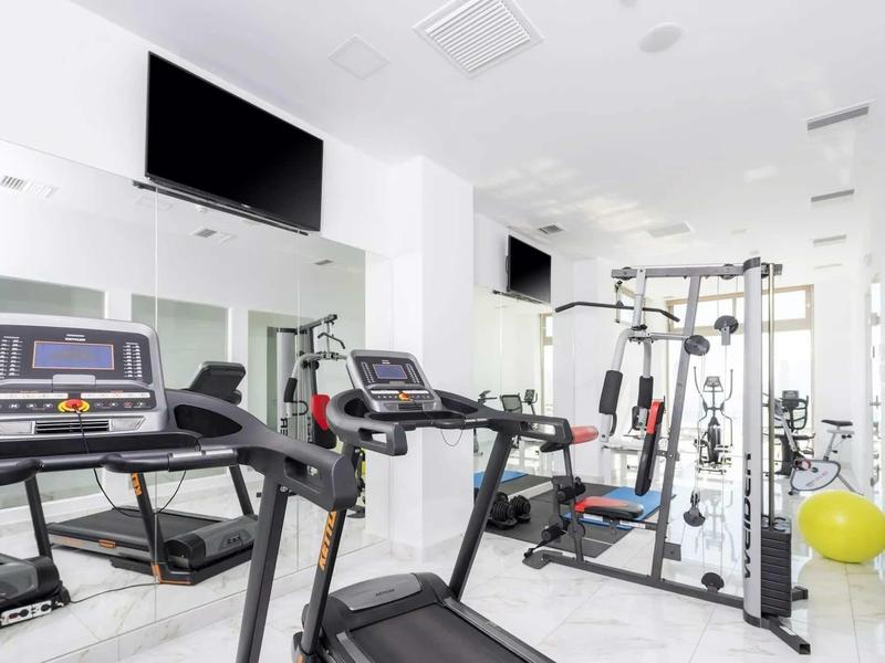 Nowoczesna siłownia z biegarkami, sprzętem siłowym i jasną marmurową podłogą.
