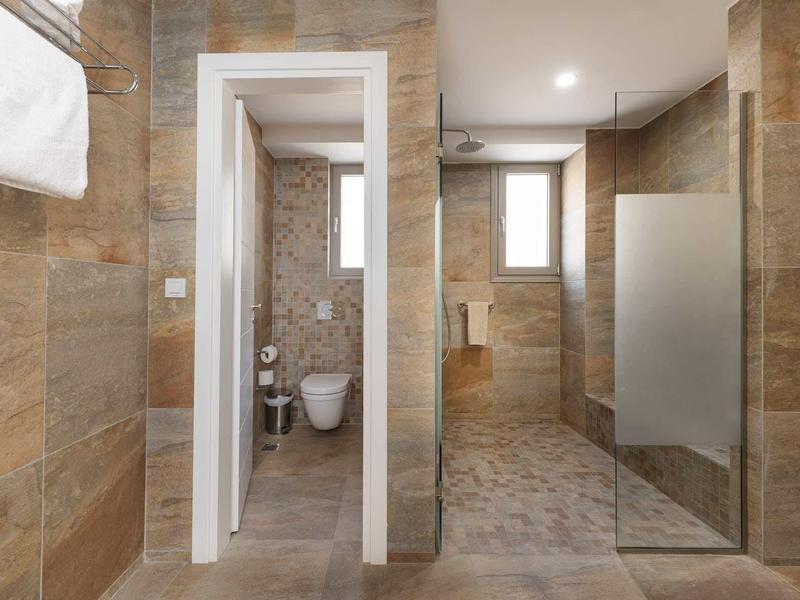 Nowoczesna łazienka z prysznicem bez brodzika, toaletą i dużymi płytkami z kamienia naturalnego.