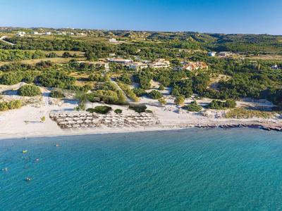 Krásná pláž s deštníky, čistou modrou vodou a zelenými kopci v pozadí.