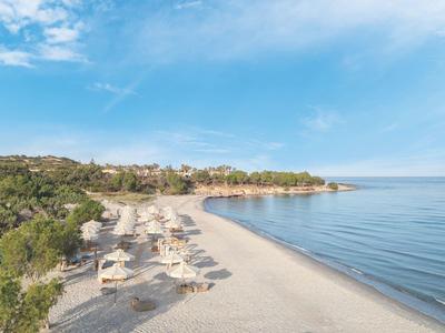 Slunečná pláž s deštníky, klidné moře a zeleň pod jasně modrou oblohou.