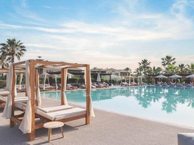 Luxusní hotelový bazén s lehátky a pergolami pod jasnou oblohou.