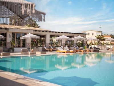 Příjemný hotelový bazén s lehátky a slunečníky pod modrou oblohou.