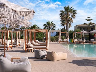 Luxuriöser Hotelpoolbereich mit Liegen, Palmen und Sonnenschirmen bei blauem Himmel.