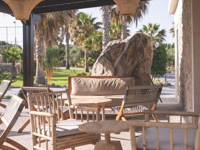 Outdoor-Sitzbereich mit Holzmöbeln und Blick auf Palmen und Felsen bei Sonnenschein