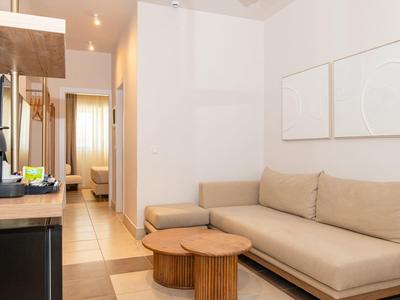 Pohodlný obývací prostor s béžovou pohovkou, dvěma kulatými dřevěnými stolky a minimalistickou výzdobou.