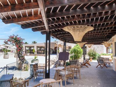 Sonnige Außenlounge mit Holzbalkendecke, Stühlen und Tischen unter Pergola.