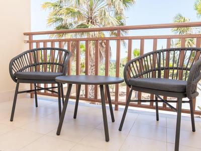 Venkovní balkon s dvěma černými židlemi a malým stolem s palmami v pozadí.