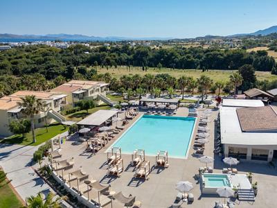 Hotel mit großem Pool, Liegestühlen und Schirmen, umgeben von Grünflächen und Bergen.