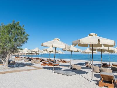 Strand mit Liegestühlen und Sonnenschirmen vor blauem Meer und klarem Himmel.