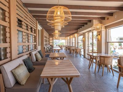 Modernes, helles Hotelrestaurant mit Holzmöbeln und gemütlichen Sitzgelegenheiten entlang großer Fenster.