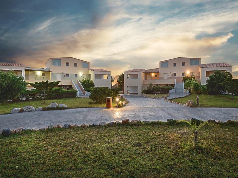 Moderní hotelové budovy s udržovanými zahradami a zataženou oblohou při západu slunce.