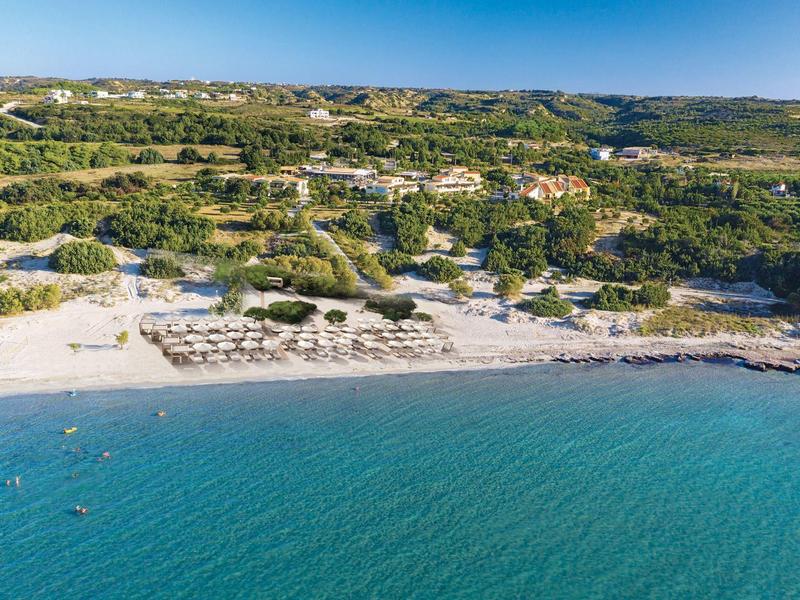 Krásná pláž s deštníky, čistou modrou vodou a zelenými kopci v pozadí.