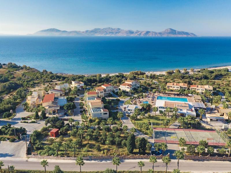 Pobřežní resort s bazény, tenisovými kurty, zelení a horami přes moře.