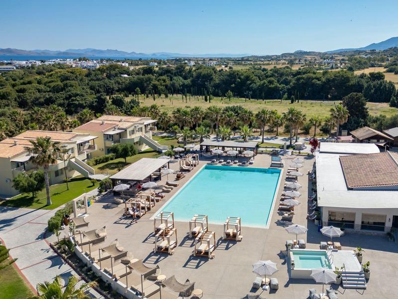 Venkovní hotelový bazén s lehátky, slunečníky a zelení pod jasnou oblohou.