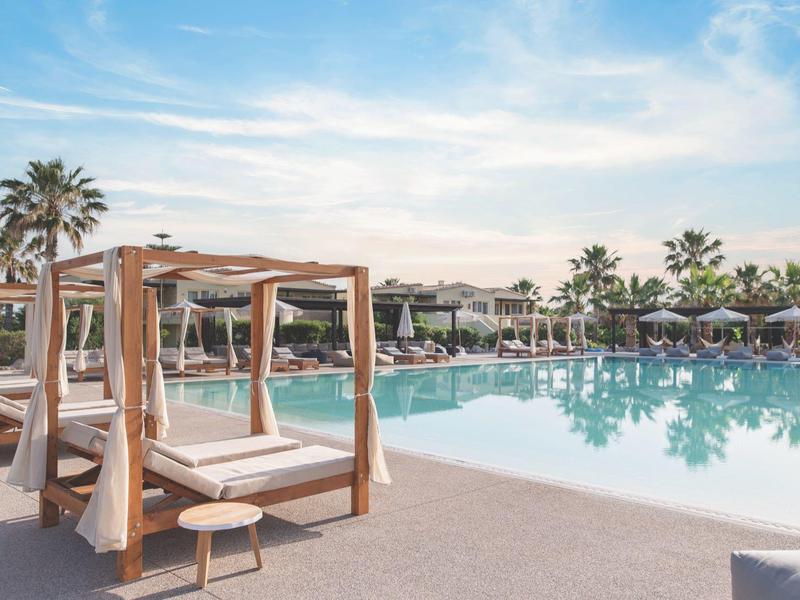 Luxusní hotelový bazén s lehátky a pergolami pod jasnou oblohou.