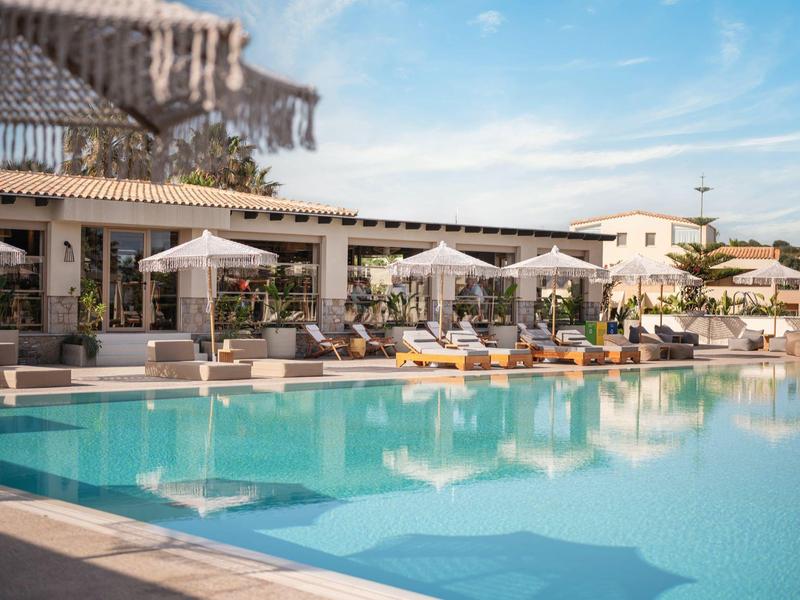 Příjemný hotelový bazén s lehátky a slunečníky pod modrou oblohou.