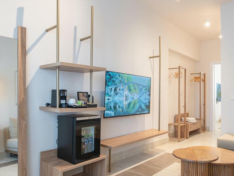 Moderní hotelový pokoj s televizí na stěně, minibarem, zrcadlovou skříní a dřevěným nábytkem.