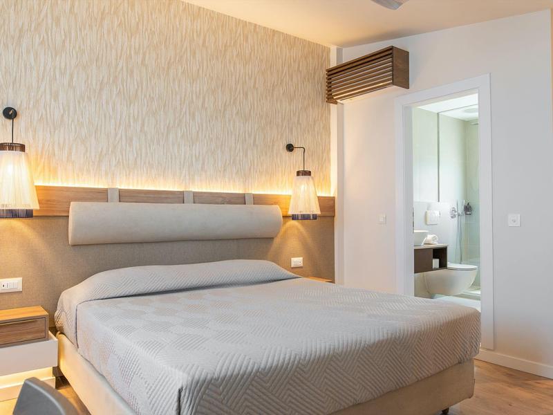 Moderní hotelový pokoj v neutrálních tónech s dveřmi do světlé koupelny.