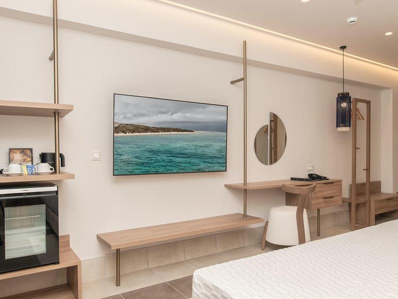 Moderní hotelový pokoj s nástěnnou TV, dřevěnými policemi, stolem, židlí a postelí.