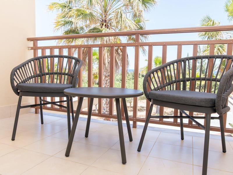 Venkovní balkon s dvěma černými židlemi a malým stolem s palmami v pozadí.