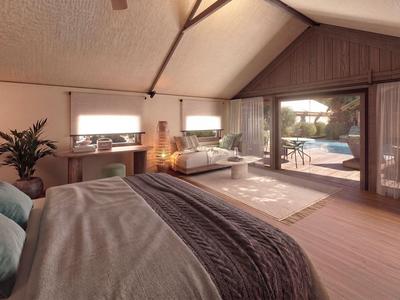 Gemütliches Hotelzimmer mit Bett, Sofa und Blick auf Terrasse und Pool bei Sonnenuntergang.