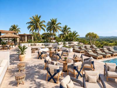 Offene Terrasse mit Lounge-Möbeln und Liegestühlen vor Palmen unter klarem Himmel.