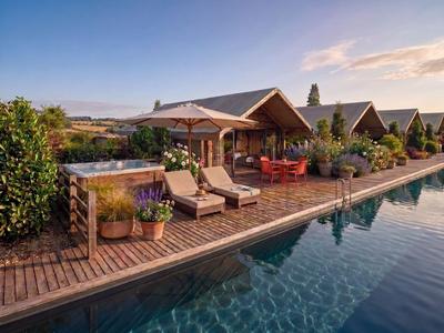 Modernes Hotel mit Holzdeck, Pool, Sonnenschirmen und Liegestühlen bei Sonnenuntergang.