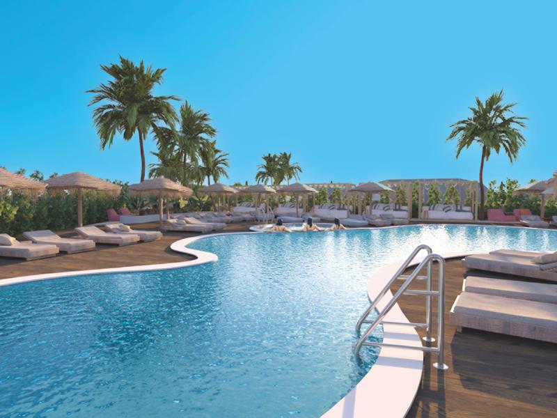 Velký bazén s lehátky a palmami pod modrou oblohou v hotelovém rezortu.