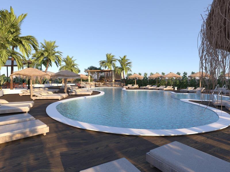 Velký kulatý bazén s lehátky a palmami pod jasnou oblohou v hotelovém resortu.