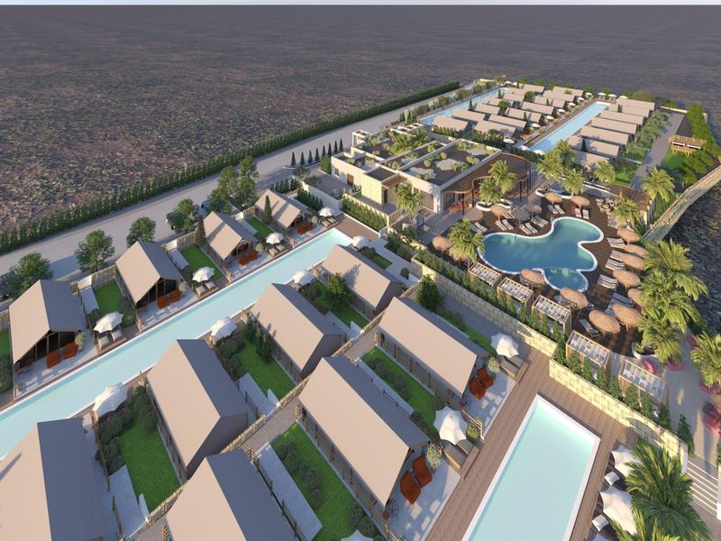 Pohled z ptačí perspektivy na resort s moderními bungalovy a velkým bazénem v tropickém prostředí.