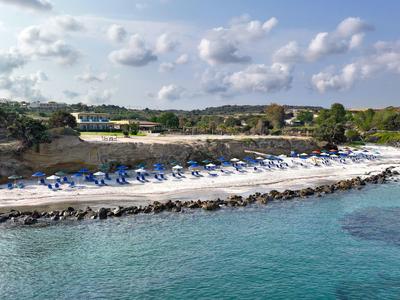 Strand mit weißen Liegestühlen und Sonnenschirmen, blaues Wasser und bewölkter Himmel.