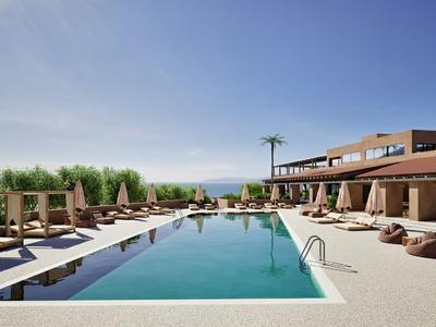 Piscina esterna moderna con lettini e pouf davanti a un hotel sotto un cielo limpido.