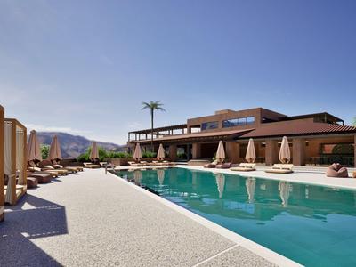 Hotelzwembad met ligbedden, parasols en bergzicht onder een heldere hemel.