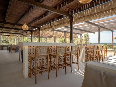 Open hotel restaurant area with wooden chairs overlooking nature and the sea.