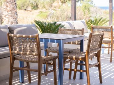 Terrace with wooden chairs and table, palm trees and sea view in the background.