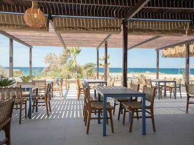 Open dining area with wooden chairs and tables, sea view in the background.