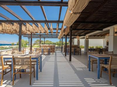 Open terrace area with dining furniture and wooden roof, sea view under clear sky.