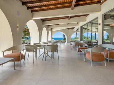 Open hotel terrace area with white arches, tables, and chairs overlooking the sea.