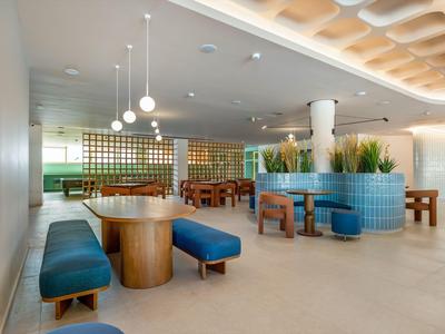 Modern hotel interior with benches, tables, plants, and stylish lighting.