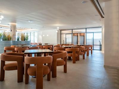 Modern dining area with brown chairs, wooden tabletops, large windows, and neutral color scheme.