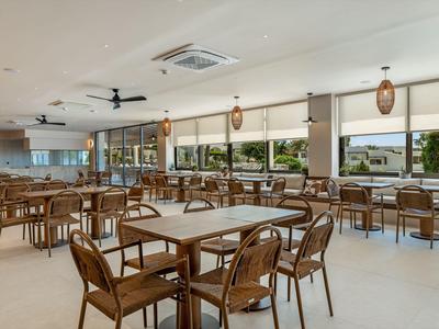 Bright dining area with wooden chairs and tables, large windows, and ceiling fan.