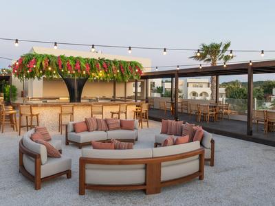 Modern outdoor hotel lounge with round sofas and a decoratively lit bar area.