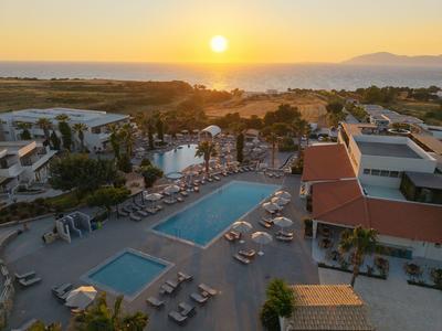 Hotel complex with pool and sun loungers by the sea at sunset.
