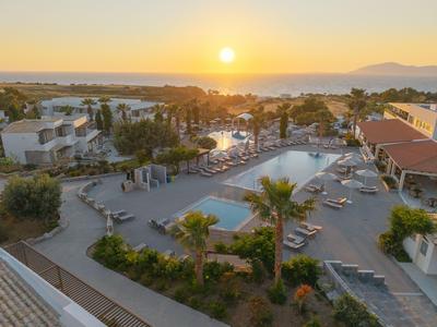 View of a hotel pool with lounge chairs at sunset by the sea.