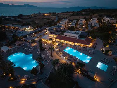 An illuminated hotel with two pools at night in a coastal area.